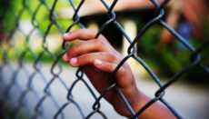 Hand in fence (Juvenile or law enforcement or jail or prison)