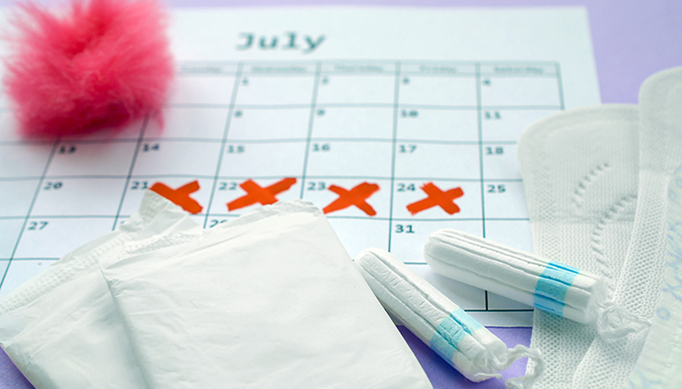 Menstrual pads and tampons on menstruation period calendar with red cross marks lies on lilac background