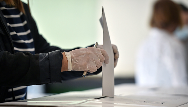 Person casting a vote into the ballot box during corona virus pa