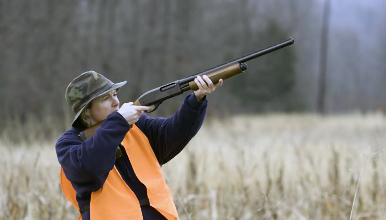 Woman shooting shotgun in field