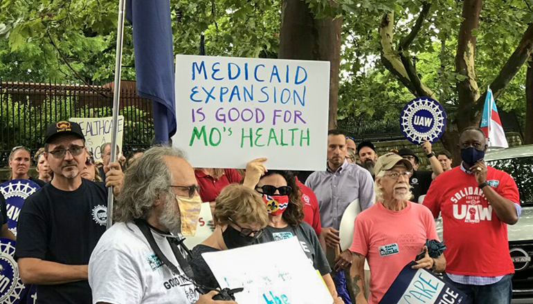 Demonstrators stand outside of the Governor’s Mansion in Jefferson City on July 1, 2021 and hold signs urging Gov. Mike Parson to fund voter-approved Medicaid expansion