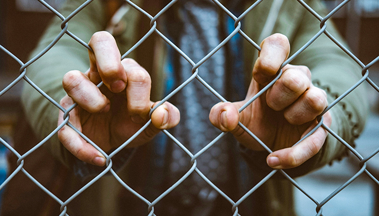 Man with fingers through fence also immigration or immigrants