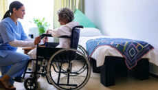 Nurse assisting patient in wheelchair in nursing home