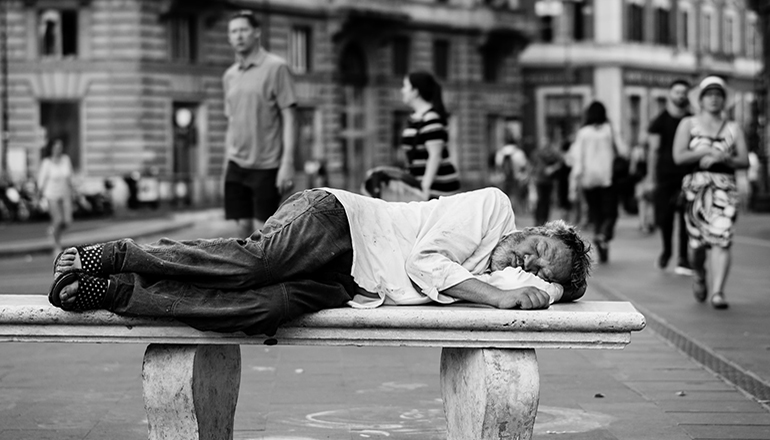 Homeless person sleeping on bench (Photo by John Moeses Bauan on Unsplash)