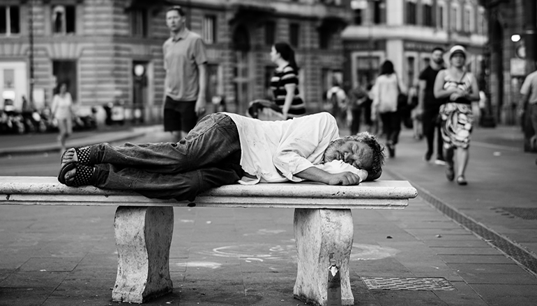 Homeless man sleeping on a bench in public (Photo by John Moeses Bauan on Unsplash)