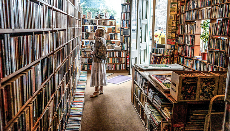 Woman browsing books in a library (Photo by John Michael Thomson on Unsplash)