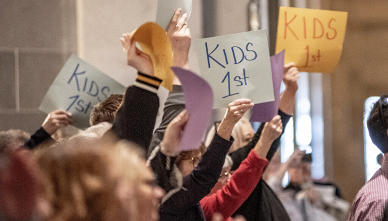Rally attendees wave signs that say kids 1st that were placed on their chairs as they applaud Missouri representatives (Annelise Hanshaw - Missouri Independent)