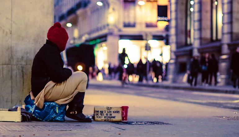 Homeless person sitting on a street corner (Photo by Ev on Unsplash)
