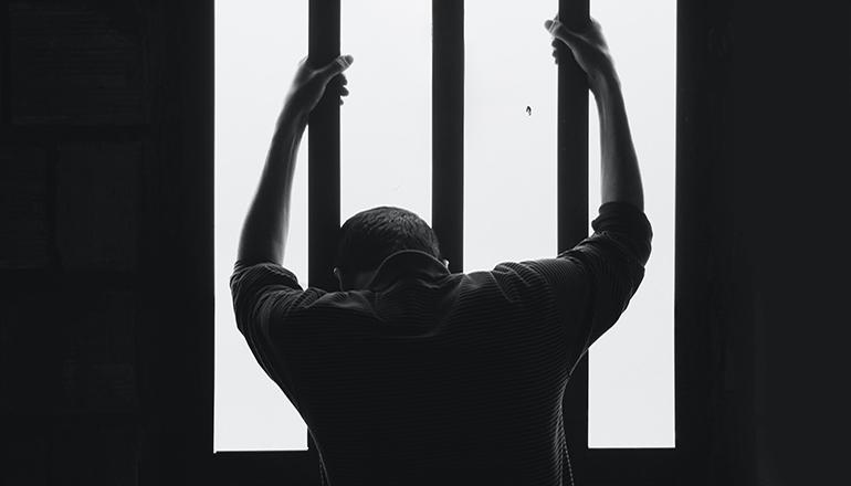 Man, inmate or prisoner in prison cell (Photo by Hasan Almasi on Unsplash)