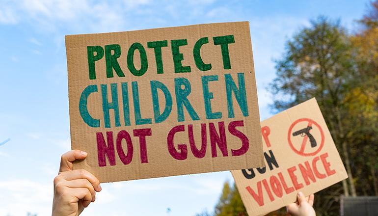 People holding protest signs protesting gun violence (Photo via Adobe Stock Images)
