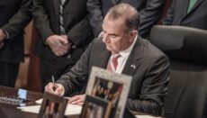 Governor Mike Kehoe signs documents at desk